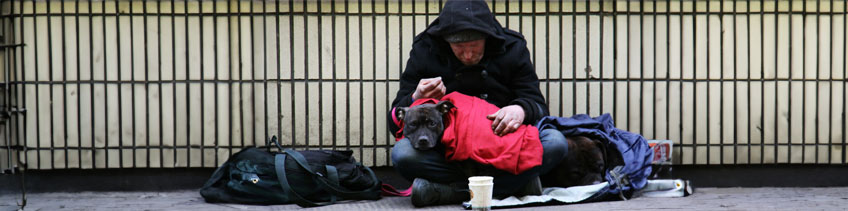 Ein Obdachloser Mann sitzt mit seinem Hund auf der Straße